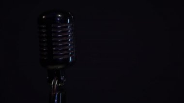 Siyah arka plandaki krom mikrofonda beyaz spot ışığı parlıyor. Profesyonel konser klasik mikrofon kaydı için ya da karanlık boş retro kulübünde seyircilerle konuşmak için..