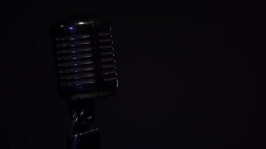 Sahne ışıkları siyah arkaplandaki tek başına krom mikrofonda sönük parlıyor. Profesyonel konser klasik mikrofon kaydı için ya da karanlık boş retro kulübünde seyircilerle konuşmak için..