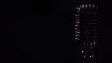 Beyaz bir adamın elleri profesyonel konser klasik mikrofonunu sola doğru kaydedebilmek için çevirir ve karanlık kulüpte bunu düzeltir. Sahne ışıkları siyah arkaplanda krom retro mikrofon üzerinde parlıyor.
