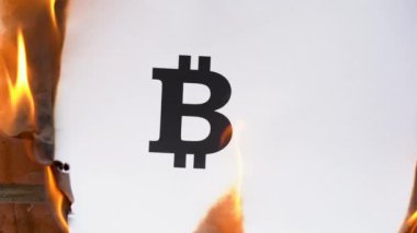 Beyaz bir A4 tablosundaki yazı turuncu bir duvarın arka planına karşı. Bitcoin 'in siyah sembolü olan kağıt yanıyor, duman çıkıyor ve küle dönüşüyor. İş konsepti.
