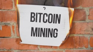 Beyaz bir A4 tablosundaki yazı turuncu bir duvarın arka planına karşı. Üzerinde Bitcoin Madencilik yazan kağıt yanıyor, duman çıkıyor ve küle dönüşüyor. İş konsepti.