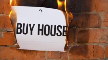 Beyaz bir A4 tablosundaki yazı turuncu bir duvarın arka planına karşı. Üzerinde Buy House yazan gazete yanıyor, duman çıkıyor ve küle dönüşüyor. İş konsepti.