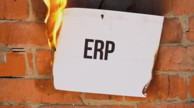 Beyaz bir A4 tablosundaki yazı turuncu bir duvarın arka planına karşı. Üzerinde Erp yazan kağıt yanıyor, duman çıkıyor ve küle dönüşüyor. İş konsepti.