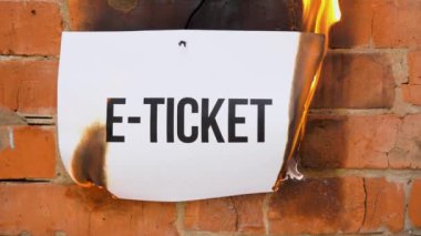Beyaz bir A4 tablosundaki yazı turuncu bir duvarın arka planına karşı. İçinde E-Ticket yazan kağıt yanıyor, duman çıkıyor ve küle dönüşüyor. İş konsepti.