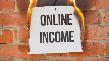 Beyaz bir A4 tablosundaki yazı turuncu bir duvarın arka planına karşı. Online Gelir 'in siyah sözcüğünün yazılı olduğu kağıt yanıyor, tütüyor ve küle dönüşüyor. İş konsepti.