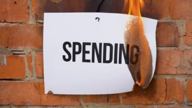 Beyaz bir A4 tablosundaki yazı turuncu bir duvarın arka planına karşı. İçinde kara kelime olan kağıt yanıyor, duman çıkıyor ve küle dönüşüyor. İş konsepti.