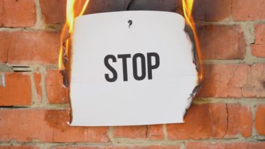 Beyaz bir A4 tablosundaki yazı turuncu bir duvarın arka planına karşı. Üzerinde siyah kelime olan kağıt yanar, duman çıkarır ve küle dönüşür. İş konsepti.