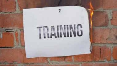 Beyaz bir A4 tablosundaki yazı turuncu bir duvarın arka planına karşı. Üzerinde siyah kelime olan gazete yakıyor, duman çıkarıyor ve küle dönüşüyor. İş konsepti.