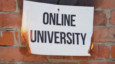 Beyaz bir A4 tablosundaki yazı turuncu bir duvarın arka planına karşı. Online Üniversitesi 'nin siyah sözcüğünün olduğu gazete yanıyor, duman çıkıyor ve küle dönüşüyor. İş konsepti.