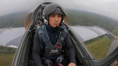 Uçaktaki uçuşlar için yeni bir pilot eğitiyorum. Gri mavi savaş uçakları bulutlu beyaz gökyüzünde yeşil alan ve orman üzerinde uçar. Kokpitten içeriye doğru. Yakından. Beyaz adam koltuğunda..