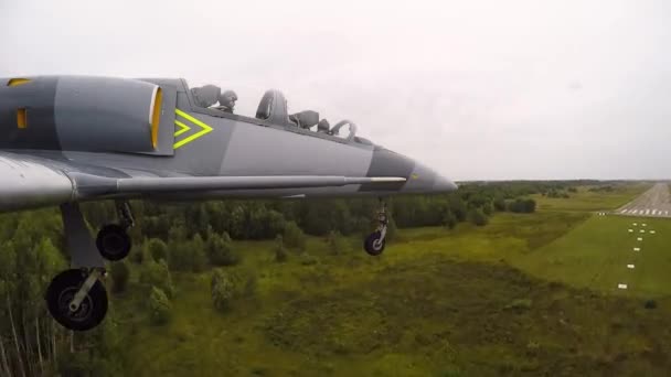 訓練用の灰色の青い戦闘機は 暗い曇りの空に対して 古い空の飛行場の着陸帯または滑走路に降ります シャーシは地面に触れています 右側の翼を上から見る — ストック動画