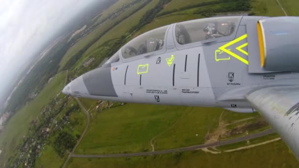 黄色の胴体要素を持つ灰色の青い戦闘機は右に傾け 暗い曇った空に対して緑のフィールドの上に高く飛ぶ 左翼端からの眺め — ストック動画