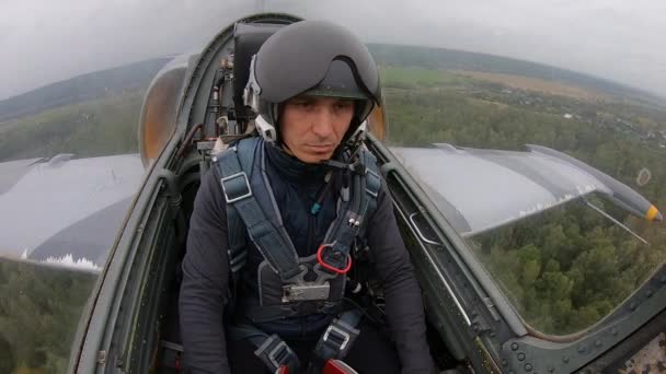 ヘルメットの白人男性 灰色の戦闘戦闘機のパイロット退屈し 曇りの曇りの空に緑のフィールドと森の上を飛んでいます コックピット近くからの眺め — ストック動画