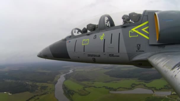 灰色的蓝色训练飞机 机身有锯齿状的机翼 朝目标飞去 一个飞行员和领航员组成的战斗机在乌云密布的天空中飞越河流和绿色的田野 从左边看近点 — 图库视频影像