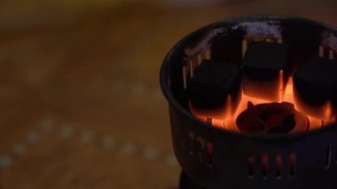 Ağdaki özel taşınabilir elektrikli ocakta kömürler yanıp tutuşuyor. 3 siyah kömür kömürü pişer ve kızarır kırmızı-sıcak spiral üzerinde sağdaki bulanık kahverengi arka planda.
