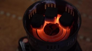 Kömürler eski bir elektrikli ocakta yanıyor ve yanıyor. 3 siyah kömür kömürü pişer ve kırmızı bir spiral üzerinde kızarır. Yakın plan bulanık kahverengi. Üst görünüm.