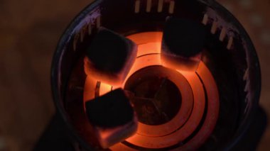 Kömürler eski bir metal elektrikli ocakta yanar ve yanar. 3 siyah kömür kömürü kızarır ve kızarır. Kırmızı-sıcak bir spiral üzerinde koyu bir arka plan üzerine yakın plan. Yukarıdan bak. Yürüyüş için nargile konsepti.