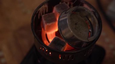 Bir kişi nargile hazırlıyor. Metal maşalı bir adam, eski bir elektrikli kontak yakıcısının üzerine közlü közler koyar. Üst Manzara. Yürüyüş için nargile konsepti.