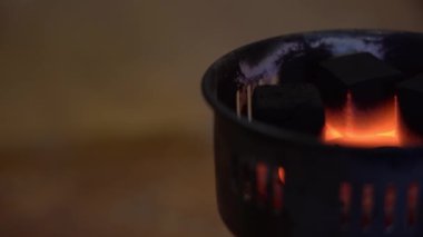 Özel taşınabilir elektrikli ocakta kömürler yanar ve yanar. 3 siyah kömür kömürü, kırmızı-sıcak bir spiral üzerindeki sıcak sıcaklıktan pişer ve kızarır. Sağ arka planda bulanık, koyu bir zemin vardır..