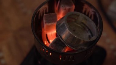 Metal maşalı bir adam kaloud 'un içine yanan kömürleri yakın kontak için taşınabilir elektrikli spiral fırına koyar. Üst Manzara. Yürüyüş için nargile konsepti.