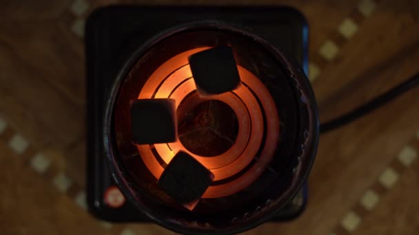 石炭は古いレトロな電気バーナーで練られ 粉砕される 3つの黒い正方形の石炭が横たわっており ぼやけた茶色の背景の上に赤い熱いオレンジ色の螺旋状に燃えます トップビュー 売春婦の概念 — ストック動画