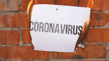 Beyaz bir A4 tablosundaki yazı turuncu bir duvarın arka planına karşı. Üzerinde siyah kelime olan CORONAVIRUS gazetesi yanıyor, duman çıkıyor ve küle dönüşüyor. Dünya Savaşı konsepti.