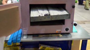 Masada açık kapısı olan kurutma ya da kireçlendirme elektrotları aygıtı kaybolur. Metal kutunun içinde birçok elektrot var. Fabrikadaki deponun arka planı üzerinde çalışan bir sürü insan var.. 