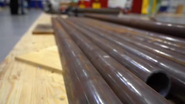 溶接用の大きな茶色の錆びた金属製の鋼管は 倉庫内の合板シートの床に置かれています 労働者はバックグラウンドで歩く 工場での作業用材料の準備 — ストック動画