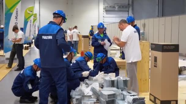 ロシア 2019年8月7日 コーカサスの労働者は 倉庫を背景に木製のパレット上のセロハンバッグに青いスーツ ヘルメットの分類や金属部品のカウントを着用してください 男は立ち メモを取り 製品を受け入れます 監査の概念 — ストック動画