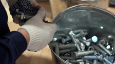 Beyaz koruyucu eldiven giyen, mavi önlüklü, metal kovadan yeni cıvatalar alıp, onları birleştirip sayan işçi. İşçi iş için malzeme topluyor. Günlük işlerin, kapalı alanların görüntülerini kapat