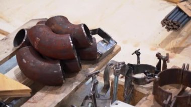 Kirli ahşap palette, paslı boruların boş kesikleri, cıvatalı kıskaçlar, metal bir cetvel, boynuz parçaları, ingiliz anahtarı. Fabrika zemininin arka planındaki kapalı manzarayı kapat.