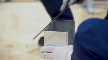 Çalışan adam mavi takım elbise giyiyor, koruyucu beyaz eldivenler giyiyor, bir dosya kullanıyor, hizalanıyor, ince metal oluğun keskin kenarlarını bulanık ışık arka planına sürtüyor. Erkek işçilerin elleri ile araçların görüntüsünü kapat.