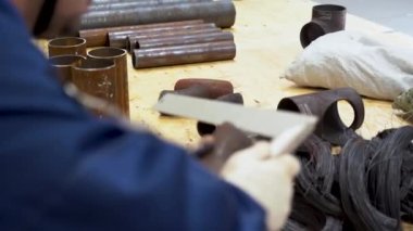 Koruyucu beyaz eldivenlerle işçi eli görüntüsünü kapat. Bir adam, inşaat alanındaki paslı bir borunun çapını, kesilmiş tel ve metal parçalarının arka planına karşı özel bir açıyla ölçüyor..