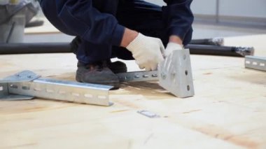 İşçi çömeliyor, mavi takım giyiyor, beyaz eldivenler manzarayı kapatıyor. İşçi fabrikada metal parçaları monte ediyor. Erkek, penseyle cıvata tutar, somunu ingiliz anahtarıyla sıkar..