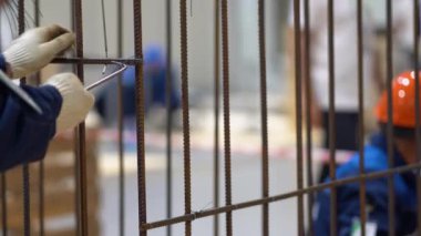 Tanınmayan bir adam metal bir yapı yapıyor. Çerçevesi demir çubuklardan yapılmış. Beyaz eldivenli işçilerin elleri paslı çubuklarla bağlanmış tellerle vidalanıyor ve fabrikada özel aletler kullanılıyor. Uzayı kopyala Görüntüyü kapat.