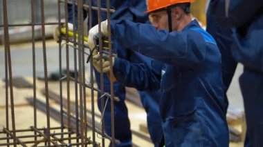 Sochi, Rusya - 07 Ağustos 2019: İki adam mavi iş kıyafetleri, miğfer, demir çubukları örgü kablosuyla çerçevelemek için beyaz eldivenler giyiyorlar. İşçi, mezura ile mesafeyi ölçer. Takım çalışması.