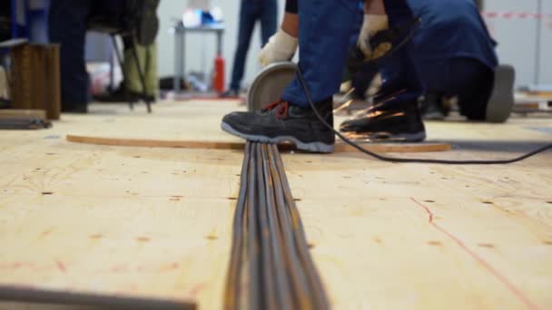 工人们穿着防护服 用研磨机工具铺在地板上的钢筋锯条 与人一起在小车间的背景下压杆 地景近景 — 图库视频影像