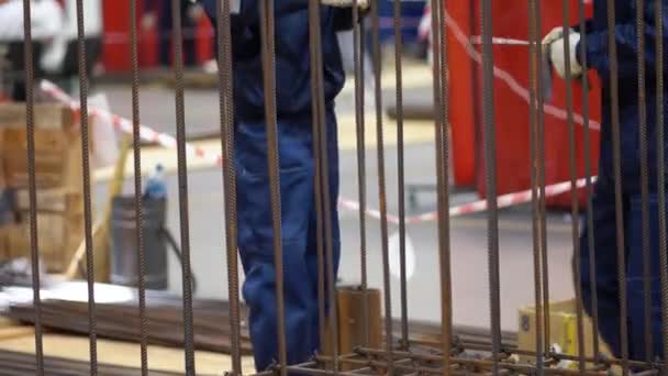 无法辨认的工人穿着蓝色工作服安装金属结构 网状钢筋棒 与金属丝拴在一起 在工厂背景下使用特殊工具近距离观察 团队精神概念 — 图库视频影像