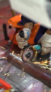 One unrecognizable worker man wear protective gloves, blue jacket uses grinder, saws and turns metal pipe with large diameter into parts at factory background close up view. Sparks fly around guy. 