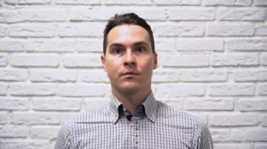 Kareli gri gömlekli yakışıklı beyaz iş adamı esmer beyaz tuğladan bir arka planda yüzüne koruyucu turkuaz bir tıbbi maske takmış ve kameraya bakıyordu..