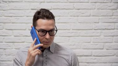 Siyah gözlüklü, gri tişörtlü, mavi telefonlu çekici, beyaz iş adamı esmer adam. Kabul etmiyor, beyaz tuğladan bir arka planda omuz silkiyor. Adam bilmediğimi söylüyor..