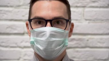 Siyah gözlüklü, koruyucu turkuaz maskeli yakışıklı esmer adam gri tuğla duvarda bir inkar hareketi ya da olumsuzluk hareketi yapıyor. Suratı asık adam, ciddi ol..