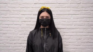 Siyah ceketli, yüzünde koruyucu tıbbi maske olan sarı bantlı yakışıklı beyaz kadın gözlerini beyaz tuğla duvara doğru açıyor. Corona virüsünden korkuyor. Korkuyu hisseder.