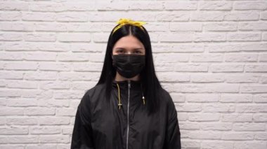 Siyah koruyucu maske takmış, yüzünde sevinçle el ele dans eden beyaz tuğla duvarda mutlulukla zıplayan sevimli Çinli bir kadın. Corona virüsüne karşı zaferin işareti..