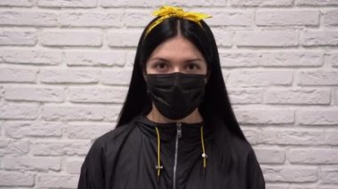Yüzünde koruyucu siyah maske takan beyaz tuğladan duvar arkası tehlikesinden korkan beyaz ceketli güzel bir beyaz kadın. Kız korona virüsünden korkuyor.. 
