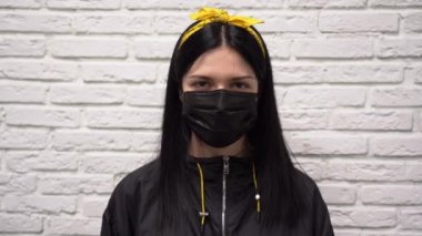 Siyah ceketli, uzun saçlı, sarı bantlı, yüzünde koruyucu maske olan genç ve yakışıklı bir kız gri tuğlalı duvarın arka planında bir inkar hareketi ya da olumsuzluk yapıyor. Kadın hayır diyor..