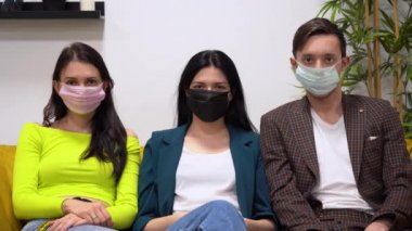 Resmi takım elbiseli beyaz insanlar oturur ve virüsün koruyucu tıbbi maskelerini çıkarırlar. Guy ve iki kız covid-19 virüsünden ve beyaz duvar arka planındaki küresel sorundan bahsediyorlar..