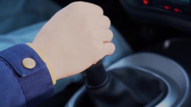 Mavi ceketli bir şoför, manuel vitesi yakın çekimde hareket ettiriyor. Adam otomatiği kontrol ediyor ve vitesi değiştiriyor, ikinci vitesten üçüncü vitese geçiyor. Erkek sürücü ve vites 2 'ye 3..