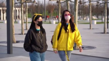 Siyah ve sarı ceketli, koruyucu tıbbi maske takan bir çift tatlı kız akşam havasında sokakta yürüyorlar. Kadınlar karantinayı ve evden çıkma yasağını umursamaz..