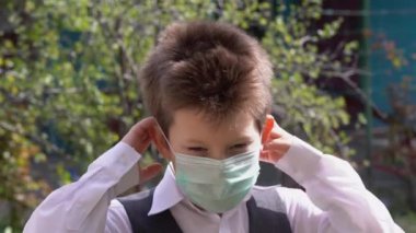 Güzel beyaz öğrenci sarışın çocuk, açık havada, yeşil güneşli bahçenin arka planında virüsten korunan turkuaz bir tıbbi maske takıyor. Covid 19 Coronavirus Koruma Konsepti.